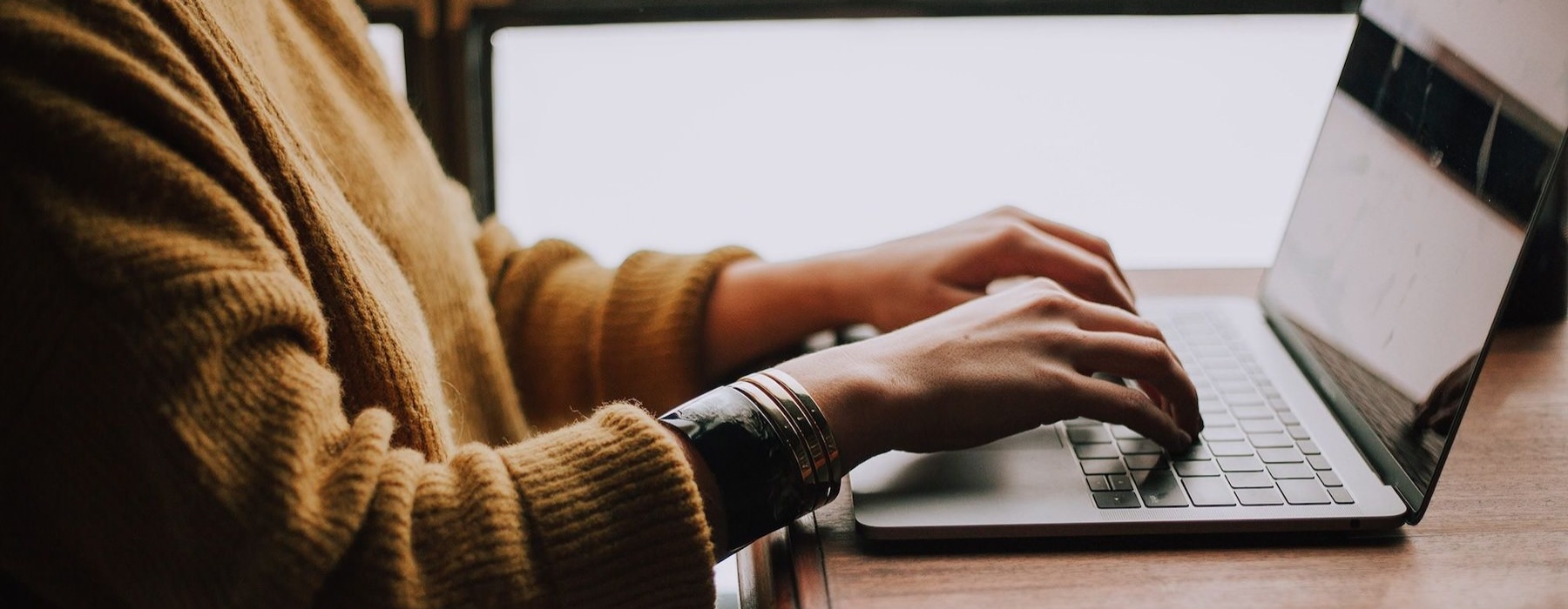 woman types on her laptop near large window